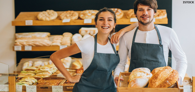 Two bakers holding fresh loaves in a bakery shop