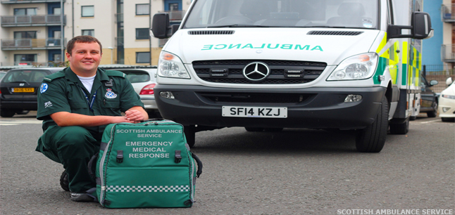 Paramedic wearing uniform, crouching in front of ambulance
