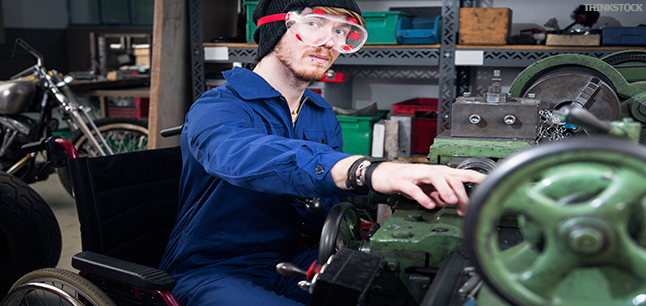 Mechanic in wheelchair wearing safety goggles, working on turning lathe