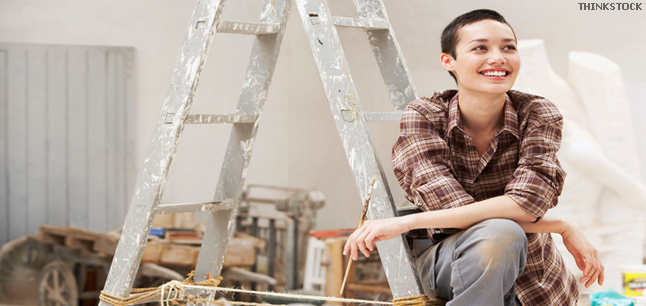 Smiling young female painter sitting on ladder